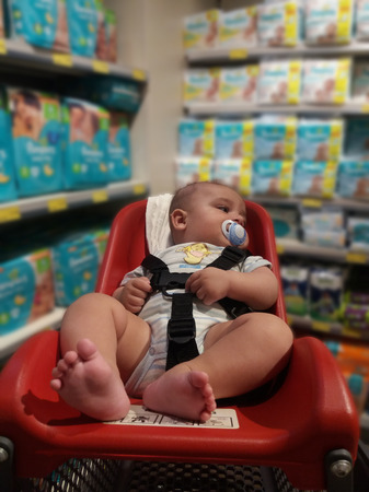 four months old baby boy in supermarket trolli for babyes in front of shelfs with baby googiesの写真素材