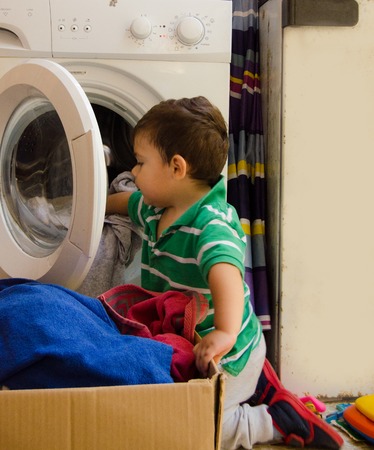 One and the half years old baby boy helping his mom by putting clothes in washing machineの写真素材