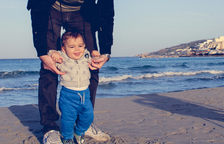 Daddy and baby boy on the sandy beach autumn, face expresion of happy familyの写真素材