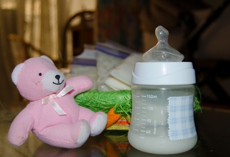 fresh expresed breast milk in baby bottle, pink teddy bear and frozen breast milk in storage bags in background, breastfeeding conceptの写真素材