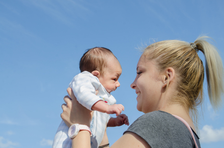 young blond mom holding one month old baby boy, blue sky, sunny day Mellieha Maltaの写真素材