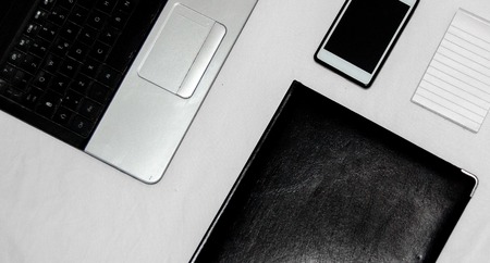 White office desk table with blank notebook, laptop and other office supplies. Top view with copy...