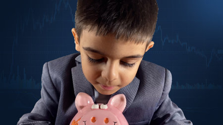 Kid in a suit looking down at the piggy bank. Stock market chart in the background. Financial education, savings for kids concept. High quality photoの写真素材