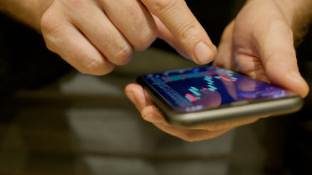 Stock market candlestick chart view on the phone in hands of a man in front of monitor with chart....