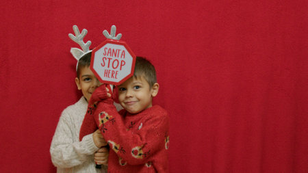 Cute kids brothers hugging and showing santa stop here sign. Christmas celebration and happy family....