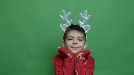 Cute boy with christmas headbank reindeer antlers posing isolated on green background. High quality photoの写真素材