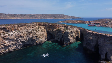Aerial view of the sea caves of Cominotto uninhabited island near Comino, Maltese islands. Seagull flying in the frame. High quality photoの写真素材