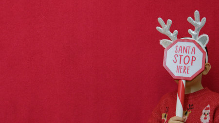 Cute boy with dear antlers holding Santa stop here sign. Cristmas background. High quality photo