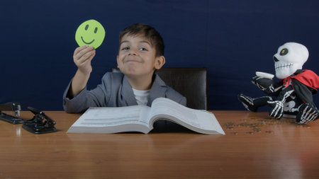 A joyful young boy in formal attire displays a smiling face, accompanied by an open book and a playful skeleton puppet, creating a humorous and cheerful workspace environment.の写真素材