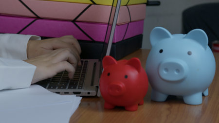 Red and blue piggy banks placed near a person typing on a laptop, symbolizing savings and planning. High quality photoの写真素材