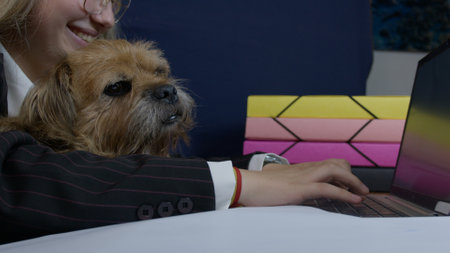 A vibrant office setting features a dog accompanying its owner while working at a laptop. The scene highlights companionship and a warm, productive work environment.の写真素材