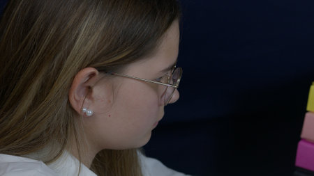 A woman sits at a workspace, deeply concentrating on her task, showcasing attentiveness and focus. She wears glasses and is surrounded by a professional setup, highlighting productivity and dedication.の写真素材