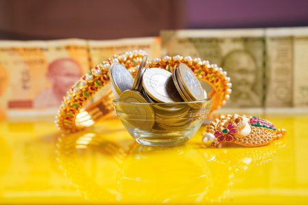 Gold bangles and indian rupees coins in bowl on yellow backgroundの写真素材