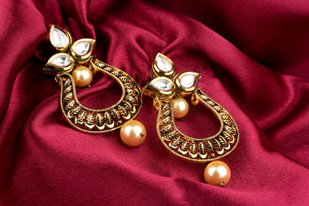 Beautiful Golden pair of earrings Diamonds gemstones on a red satin background. Luxury female jewelry, Indian traditional jewellery, kundan earring,Bridal Gold earrings wedding jewelleryの写真素材