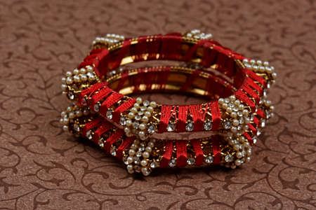Indian Red Bangles. Bracelet with threads,diamonds and pearls on a textured background, Indian...