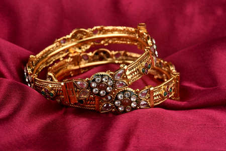 Indian golden Bangles. Bracelet with diamonds and stones on a red satin background, Indian...