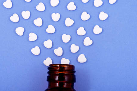 Heart shaped pills from bottle glass on a blue background. Medicines that help people.の写真素材