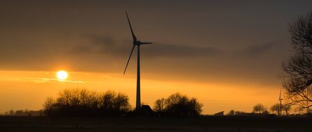 Sunset over the land. Wind turbines stand in the landscape of Nordfriesland. It seems as though the wind turbines in Nordfriesland watch the sunset - Wesselburen, Germanyの写真素材