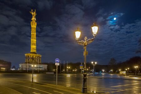 The moon looks at the illuminated Victory Column. Lanterns shine on the street in front of the Victory Column - Berlin, Germanyの写真素材