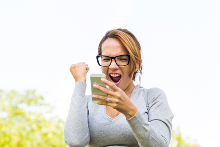 beautiful woman celebrating success news with arms up in a parkの写真素材