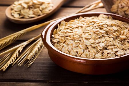 Oat flakes, uncooked oats in bowl with wooden spoon and wheat ears. Concept of healthy eating, vegan food, healthy food, breakfast.の写真素材