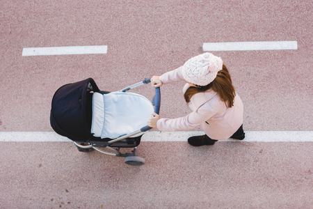 Portrait of young mother with baby carriage walking in parkの写真素材