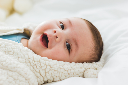 Portrait of an adorable 3 month old baby smiling lying in a bed of white sheetsの写真素材