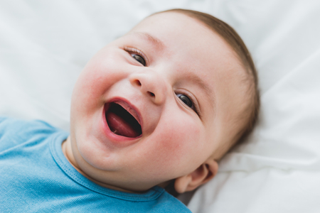 Portrait of an adorable 3 month old baby smiling lying in a bed of white sheetsの写真素材