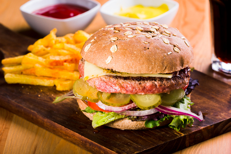 Combination of hamburger with cheese and pickles accompanied by potatoes, cola, tomato sauce and mustardの写真素材