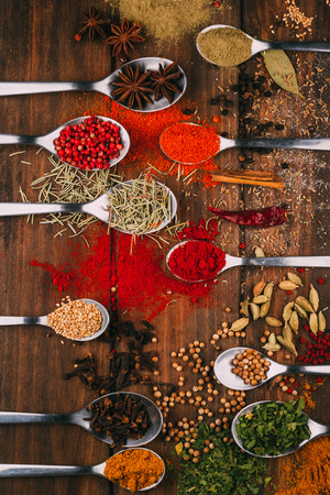 Top view of wooden table full of spices in spoons, you can see the most popular condiments and seasonersの写真素材