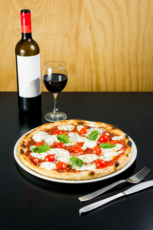 Delicious pizza served with a bottle and glass of red wine in a restaurantの写真素材