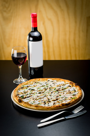 Delicious pizza served with a bottle and glass of red wine in a restaurantの写真素材