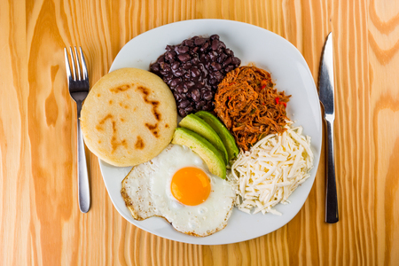 Venezuelan breakfast of arepa, fried egg, black beans, mechada meat, white cheese and avocadoの写真素材