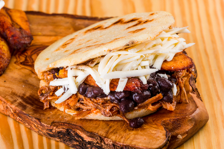 Delicious arepa stuffed with white cheese, fried plantain, roasted meat and black beans, Latin American foodの写真素材