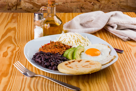 Venezuelan breakfast of arepa, fried egg, black beans, mechada meat, white cheese and avocadoの写真素材