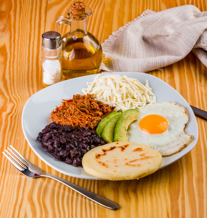 Venezuelan breakfast of arepa, fried egg, black beans, mechada meat, white cheese and avocadoの写真素材