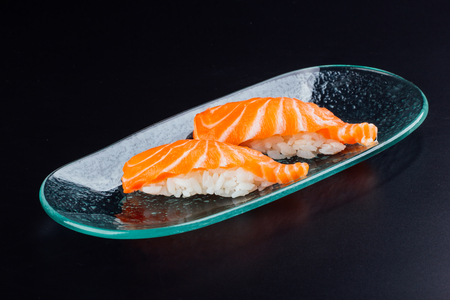 Plate with two fresh salmon nigiris on black backgroundの写真素材