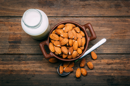Top view of wooden table with Almond milk and several almonds in a bowlの写真素材