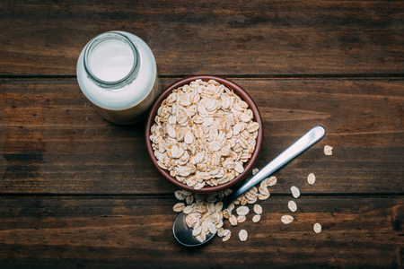 Oat milk and bowl with oat flakes on a wood backgroundの写真素材