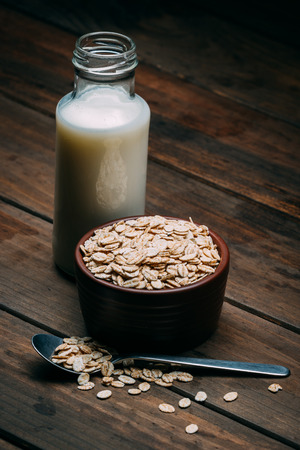 Oat milk and bowl with oat flakes on a wood backgroundの写真素材