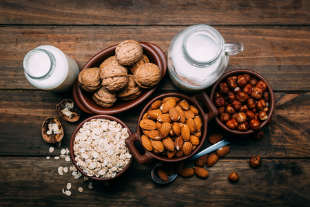 Different types of vegan milk, almond milk, oat milk, hazelnut milk and walnut milk on a wood backgroundの写真素材