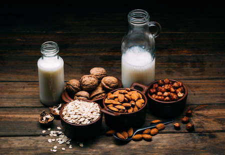 Different types of vegan milk, almond milk, oat milk, hazelnut milk and walnut milk on a wood backgroundの写真素材