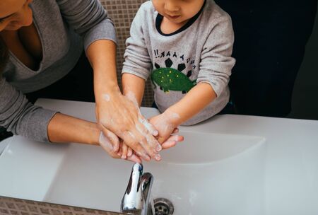 Mother and son washing their hands with soap and water in home bathroom. Cleaning hand hygiene to...