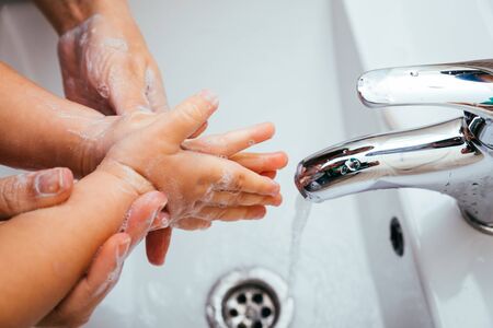 Mother and son washing their hands with soap and water in home bathroom. Cleaning hand hygiene to...