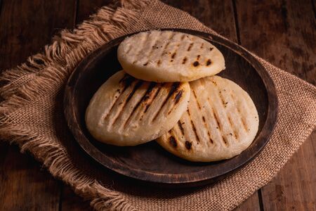 Top view of a group of traditional Latin American arepas on a wooden background.Arepas are a...