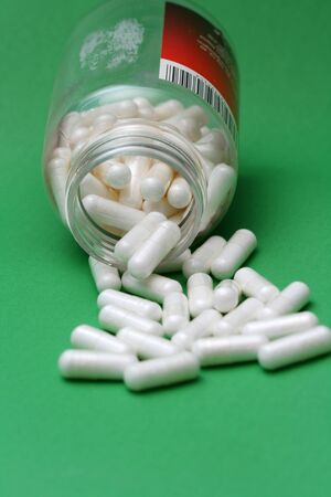 Pills spilling out of pill bottle on green backの写真素材