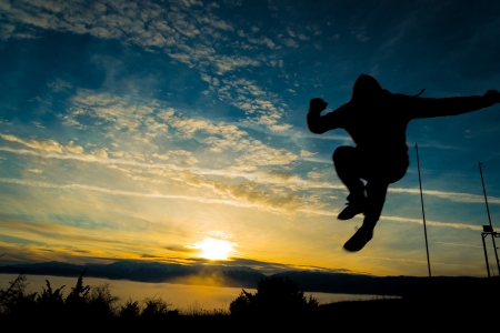 Silhouette of happy man jumping on sunsetの写真素材