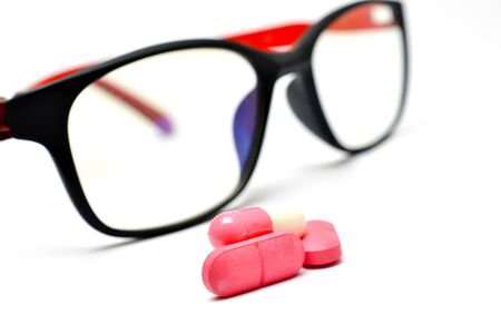 pink pills in front of eyeglasses on white backgroundの写真素材
