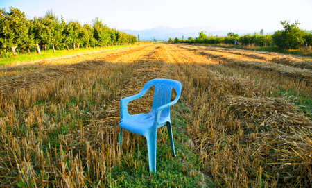 broken plastic garden chair in harvested wheat field, imageの写真素材