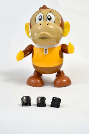 NFT text with used black computer keys in front of plastic monkey toy on white background.の写真素材